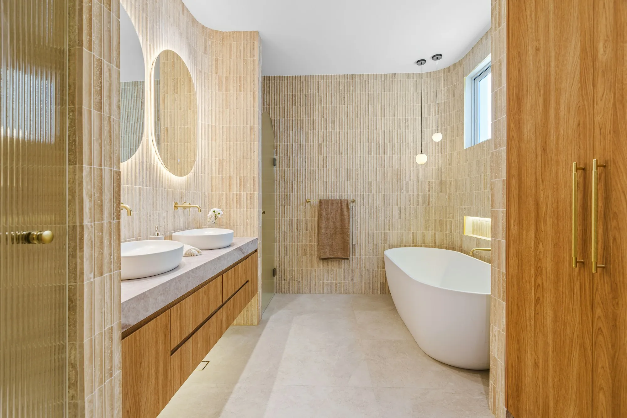 Remodeled bathroom with a freestanding tub, wood vanity and warm textured wall tile